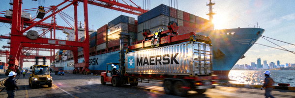 国际货运集装箱货轮在港口装卸货物的繁忙场景，背景有龙门吊